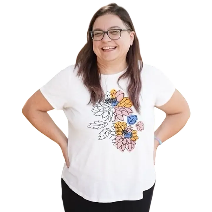 Linda smiles openly directly at you. She has dark glasses and dark brown hair with pastel purple tips, and is wearing black jeans and a white t-shirt that has a friendly flower design.