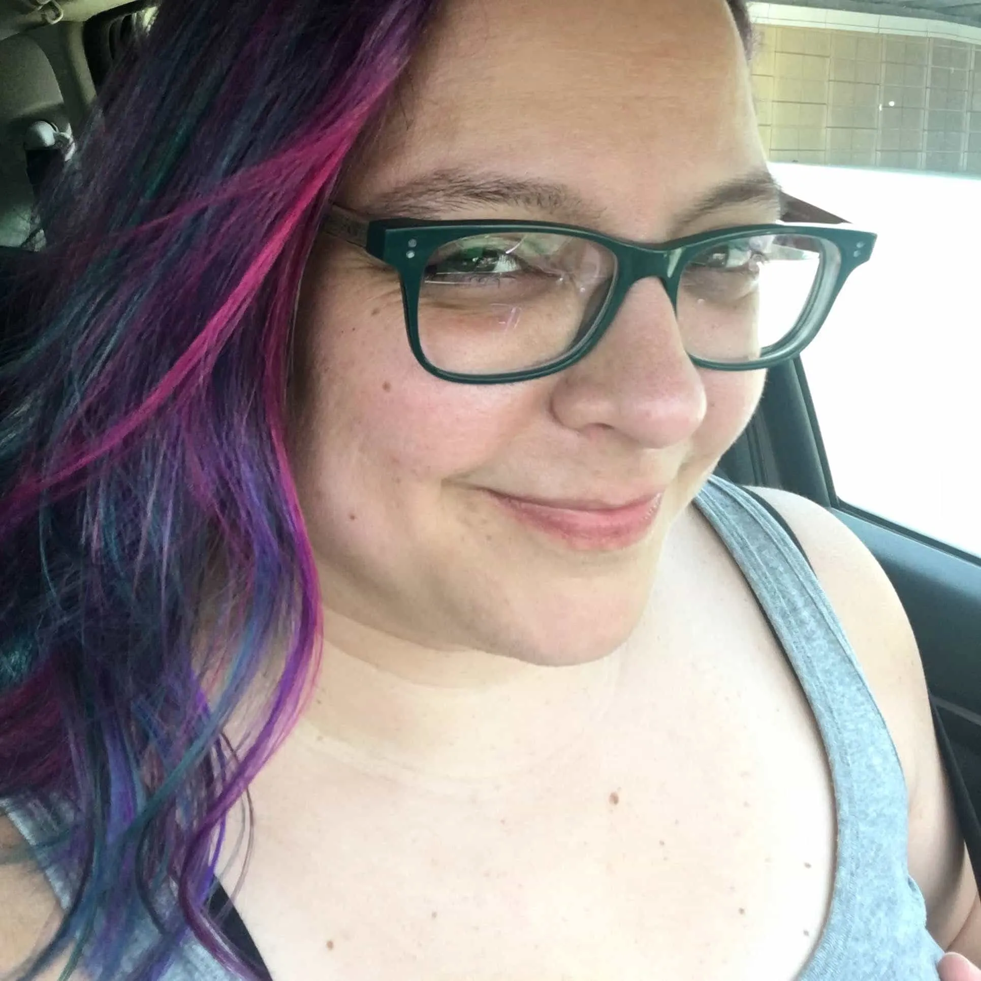 Woman with blue, purple, pink, and brown hair, brown eyes, green glasses, and a confident smirk.